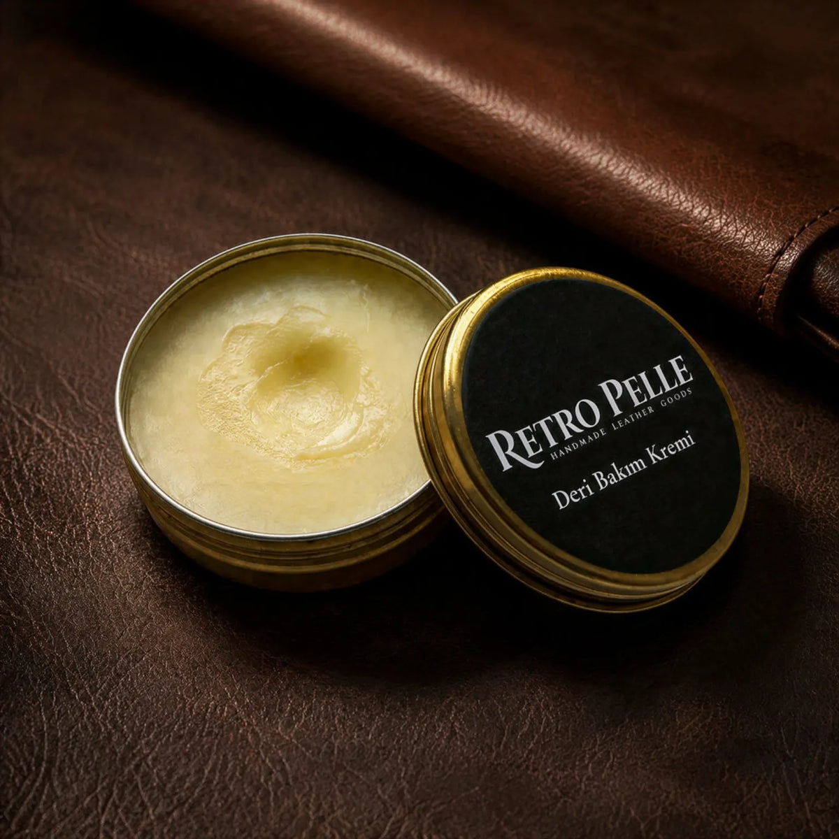 Kahverengi deri üzerinde açık kutuda Retro Pelle deri bakım kremi ve siyah etiketli altın renkli metal kapak.